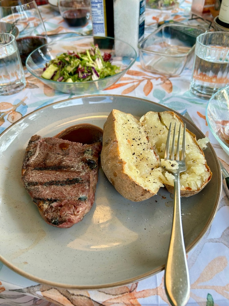 A grey dinner plate holds a large steak and a baked potato.